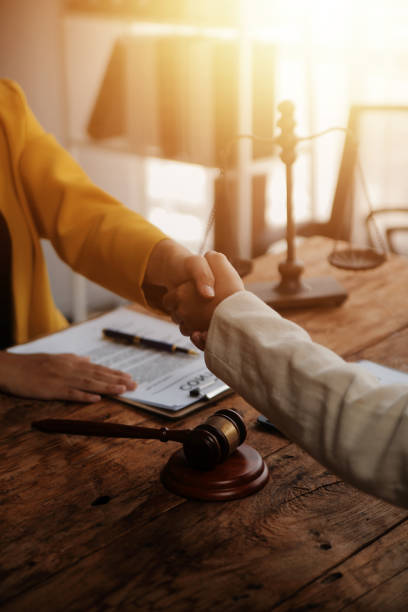 Lawyer shaking hands with a client making about documents, contracts, agreements, cooperation agreements with a female client at the lawyer's desk and a hammer at the table.
